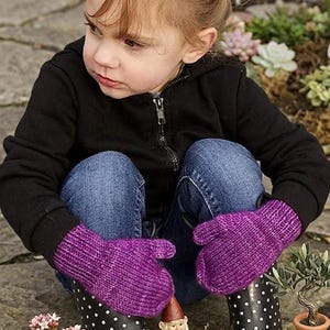 Peut inclure: Une paire de moufles tricotées d'un violet vif, dotées d'un poignet côtelé et d'une finition en fil texturé. Les moufles sont portées aux mains, mettant en valeur la couleur violette profonde et la construction en tricot épais et chaud.