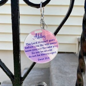 May include: A pink and purple round keychain with the name Abby and the Bible verse "The Lord Himself goes before you: He will never leave you nor forsake you. Do not be afraid: do not be discouraged. Deut 31:8"