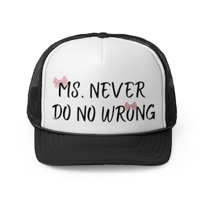 Op de afbeelding: Een zwart-witte truckercap met een wit voorpaneel. Het voorpaneel heeft de tekst "Ms. Never Do No Wrong" in zwarte tekst met twee roze strikken aan weerszijden van de tekst.