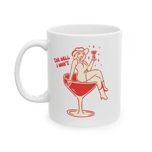 May include: White ceramic mug featuring a red illustration of a woman wearing a cowboy hat, perched inside a martini glass. The text "The Hell I Won't" is printed in red on the mug.