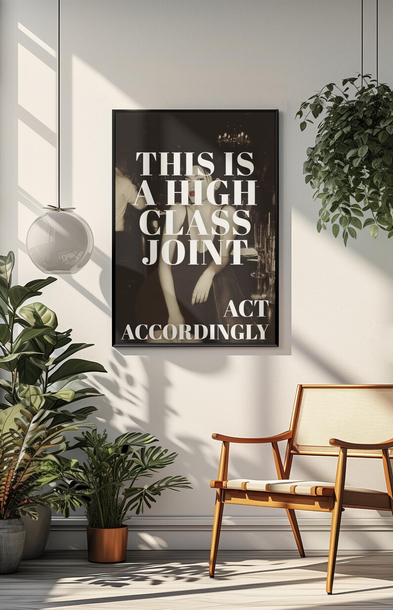 May include: Black framed poster with the text "THIS IS A HIGH CLASS JOINT ACT ACCORDINGLY" in white. The poster is hanging on a white wall, with a wooden chair and plants in the foreground. The image has a vintage aesthetic.