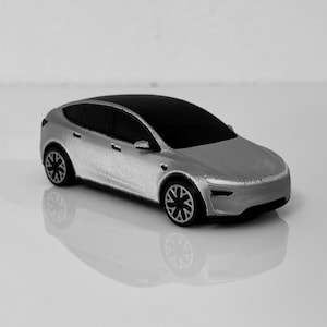 Peut inclure: Une voiture miniature argentée dotée d'une carrosserie aérodynamique, d'un toit noir, de vitres teintées sombres et de roues détaillées à rayons multiples. Le véhicule présente un design moderne avec une finition lisse et une surface métallique.