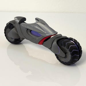 以下が含まれることがあります： 黒いタイヤと赤と紫のアクセントが付いた、未来的なグレーのオートバイのおもちゃ。 おもちゃのオートバイは、ロープロファイルのスリムなデザインで、プラスチック製です。 タイヤにはユニークなトレッドパターンがあります。
