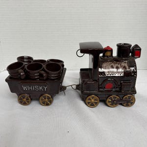 以下が含まれることがあります： 茶色の陶器製の列車セット。機関車と「WHISKY」と書かれた客車があります。客車には6つの小さな茶色のマグカップが入っています。列車は金色の車輪と赤いアクセントが特徴です。ユニークなバーウェアセット。