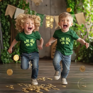 May include: Two young boys wearing green shirts with shamrock designs jump in the air, surrounded by gold coins. They are both smiling and laughing.