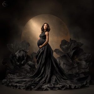 May include: A pregnant person in a flowing black gown, posing in front of a large, golden-hued backdrop. The dress features a halter neckline and a long, trailing skirt. Large, dark floral accents frame the subject, creating a dramatic and elegant portrait.