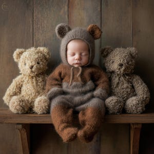Puede incluir: Un bebé dormido con un conjunto de punto con temática de oso marrón y gris con capucha y orejas, flanqueado por dos osos de peluche en un estante de madera. Los osos son de color marrón claro y gris. El fondo es una pared de madera rústica.
