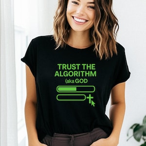Op de afbeelding: Zwart T-shirt met de groene tekst "TRUST THE ALGORITHM (aka GOD)". Het ontwerp bevat een laadbalkgrafiek en een cursor met een kruissymbool. Het T-shirt wordt door een persoon gedragen.