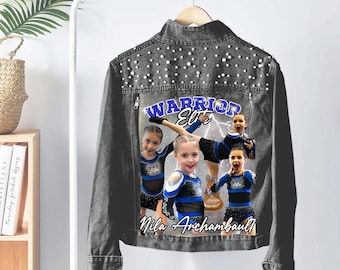 May include: A dark grey denim jacket with pearl detailing on the shoulders. The back displays a graphic of cheerleaders, the text "Warrior Elite", and the name "Mila Archambault".