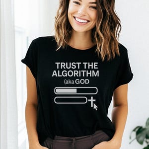 Peut inclure: T-shirt noir avec l'inscription blanche "TRUST THE ALGORITHM (aka GOD)". Le motif comprend deux barres horizontales, dont une partiellement remplie, et un curseur avec une croix. Le t-shirt est porté par une personne.