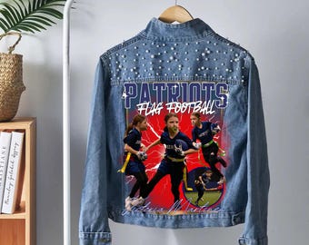 May include: A light blue denim jacket featuring a back graphic of three flag football players and the text Patriots Flag Football. The upper back panel is embellished with white faux pearls. The jacket has a collar, long sleeves, and button cuffs.