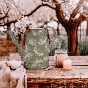 Könnte beinhalten: Eine dekorative Gießkanne mit floralem Muster, gefüllt mit weißen Blumen, steht auf einem Holztisch. Daneben befinden sich ein kleines Glas mit einer Kerze und ein Glas mit einer weißen Flüssigkeit. Der Text "Digital Mockup" ist sichtbar.