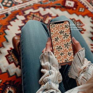 Puede incluir: Una persona sostiene un teléfono inteligente con un patrón floral en la pantalla. El teléfono es de color oro rosa y tiene un fondo blanco. El texto en la pantalla dice "Digital Mockup PSD smart object for Photoshop".