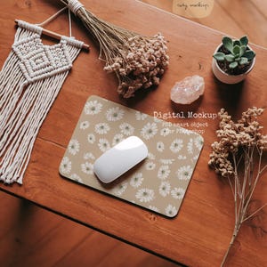 Puede incluir: Una alfombrilla de ratón beige con un patrón de margaritas blancas y un ratón inalámbrico blanco en la parte superior. La alfombrilla de ratón está sobre una mesa de madera con flores secas, un cristal y una pequeña maceta de suculentas.
