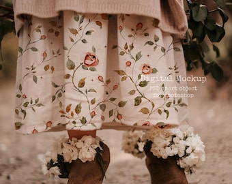 May include: A person wearing a beige sweater and a floral print skirt with roses and vines. The person is wearing brown suede boots adorned with white flowers. The image has a soft, natural aesthetic.