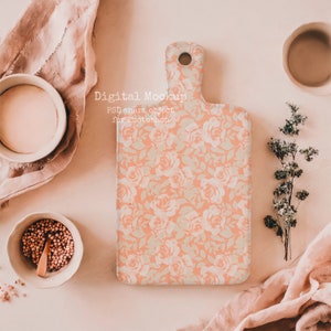 May include: A peach-colored cutting board with a floral rose pattern, a handle, and a hole for hanging. The words "Digital Mockup" and "PSD smart object for Photoshop" are printed on the board. The board is surrounded by bowls and fabric.