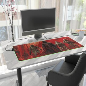 May include: A rectangular desk mat featuring a vibrant red graphic illustration of Darth Vader and several Stormtroopers in a forest setting. The mat has a thin, illuminated green border along its edge and a black power cord extending from the left side.