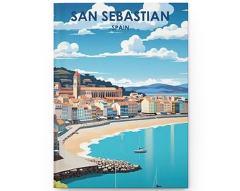 May include: A hardcover journal featuring a colorful illustration of San Sebastian, Spain. The image depicts a coastal town with buildings, a beach, and boats on the water under a blue sky with clouds. The text "SAN SEBASTIAN SPAIN" is at the top.