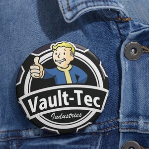 May include: A black and white button with a cartoon character giving a thumbs up. The character is wearing a blue jumpsuit and a yellow undershirt. The text "Vault-Tec Industries" is written in white on a black background.