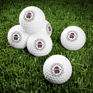 May include: Five white golf balls with a black and red design. The design features a cartoon character with a helmet and the text "THE BAD BATCH CLONE FORCE 99".