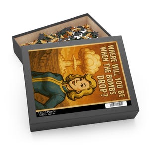 May include: A 16x20 inch puzzle in a black box. The puzzle features a retro illustration of a woman in a blue and yellow jumpsuit with a mushroom cloud in the background. Text on the puzzle reads, "WHERE WILL YOU BE WHEN THE BOMBS DROP?" and "500 pcs Ages 9+".