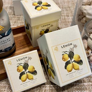 May include: Cream-colored boxes of lemon-scented soap with a botanical illustration of lemons and blossoms. The boxes are labeled "LEMON" and "FINE VEGETABLE SOAP MADE IN ITALY". The total net weight is 15.9 oz.