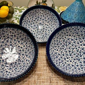 Puede incluir: Tres cuencos de cerámica azul y blanco con un patrón floral. Los cuencos tienen un borde de cuentas y están dispuestos sobre una superficie tejida.