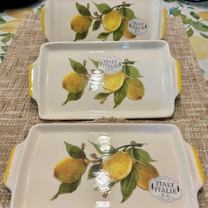 May include: Three rectangular serving platters. Each white platter features a lemon branch design with yellow lemons and green leaves. The platters have yellow handles and a sticker that says "Made in Italie".