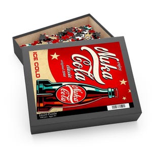 May include: A gray puzzle box with a red and cream-colored graphic of a Nuka Cola bottle. The box is open, revealing puzzle pieces. Text on the box includes "Nuka Cola", "Ice Cold", and "16x20 Puzzle".