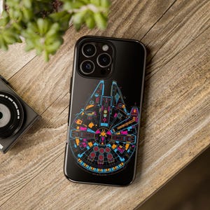 Puede incluir: Una funda de teléfono negra con un gráfico colorido del Halcón Milenario de Star Wars. La funda tiene un fondo negro con un diseño azul, rosa, amarillo y naranja.