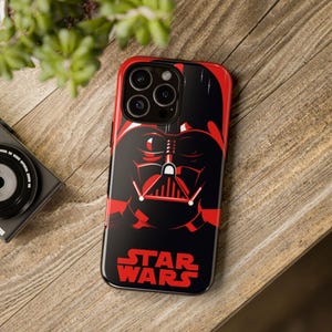 Peut inclure: Une coque de téléphone noire et rouge sur le thème de Star Wars. La coque présente un gros plan du visage de Dark Vador avec le texte "Star Wars" en dessous.