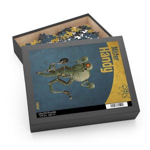 May include: A 16x20 inch puzzle box with the image of a green robot named Mister Handy on a blue background. The box is open, revealing puzzle pieces. The box also has the text "Fallout" and "500 pcs Ages 9+".