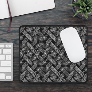Pode incluir: Mousepad preto e branco com um design de nó celta. O mousepad tem uma borda preta e um mouse branco está em cima.