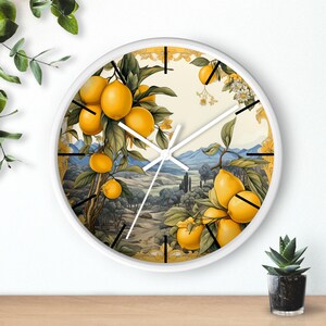 May include: White round wall clock with a lemon tree design. The clock face features a white background with black hour and minute hands. The clock is surrounded by a white frame with a gold trim. The clock face features a lemon tree with yellow lemons and green leaves. The background of the clock face features a landscape with mountains and trees.