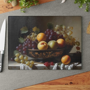 May include: A still life painting of a bowl filled with fruit. The bowl is black with gold accents and contains grapes, green plums, and yellow peaches. The bowl is sitting on a white surface with a white cloth draped over the side.