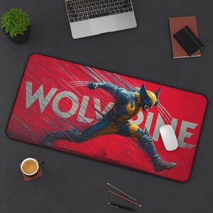 May include: A rectangular desk mat featuring a dynamic illustration of the character Wolverine in a blue and yellow suit with extended claws. The background is a vibrant red with motion lines and the word WOLVERINE printed in large white letters.