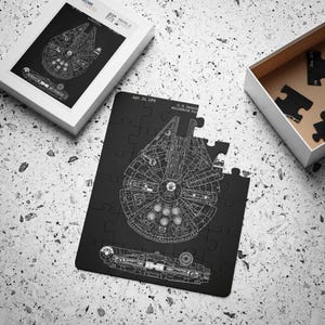 Puede incluir: Rompecabezas en blanco y negro del  Millennium Falcon, la nave espacial de Star Wars. El rompecabezas está ensamblado y muestra el plano detallado de la nave. El rompecabezas está sobre una superficie gris.