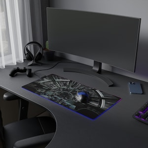 May include: A black gaming mouse pad with a futuristic design, a black gaming mouse, a black computer monitor, a black wireless controller, and a black smartphone on a black desk.