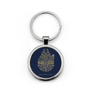 Può includere: Un portachiavi rotondo con un anello in metallo color argento e un ciondolo blu navy. Il ciondolo presenta un disegno a linee dorate di un'astronave e il testo "WHAT A PIECE OF JUNK!".