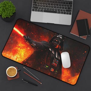 Könnte beinhalten: Eine schwarze und rote Star Wars-Mausmatte mit Darth Vader, der ein rotes Lichtschwert hält. Der Hintergrund ist in einem feurigen Orange und Gelb gehalten.