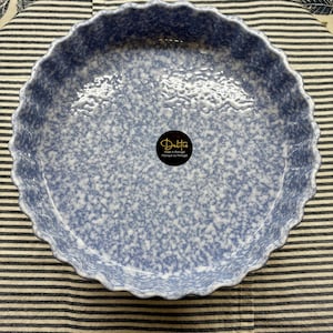 Puede incluir: Un molde para tarta redondo de cerámica azul claro con un patrón moteado y un borde festoneado. El plato tiene un acabado brillante y una etiqueta negra y dorada que dice "Deltis Made in Portugal".
