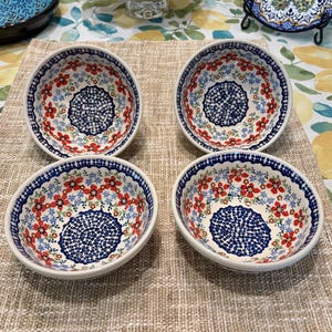 May include: Four ceramic bowls with a floral design. The bowls have a white base with a blue rim and a pattern of red flowers and blue accents. The center of each bowl features a detailed blue design.