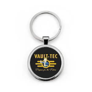 Op de afbeelding: Een ronde sleutelhanger met een zwarte achtergrond met de gele woorden "VAULT-TEC", samen met een personage dat een duim omhoog geeft. De tekst "Prepare for the Future" staat onder het logo. De sleutelhanger heeft een zilveren metalen ring.