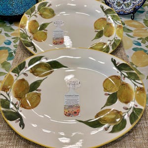 May include: Two oval ceramic serving platters with a lemon and leaf design. The plates have a white background with a yellow rim. The lemon branches are green with yellow lemons. The plates have a label that says "Italy" and "Ceramica Cuore".