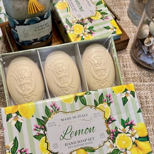 May include: A gift set of Italian lemon-scented hand soaps, with three oval soaps in a box. The box is decorated with lemon and floral designs. A jar of bath salts and a decorative box are also visible.