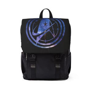 Puede incluir: Mochila negra con solapa con diseño de galaxia y emblema de estrella. La mochila tiene dos bolsillos delanteros, asa superior y correas ajustables. El diseño es una mezcla de azul, morado y blanco.