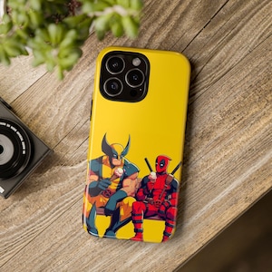 Puede incluir: Una funda de teléfono amarilla con un gráfico de Wolverine y Deadpool comiendo helado. La funda tiene un recorte para el objetivo de la cámara negro.