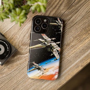 Peut inclure: Une coque de téléphone noire avec un motif de chasseur X-Wing de Star Wars. La coque présente un fond noir avec des étoiles blanches et deux chasseurs X-Wing volant en formation.