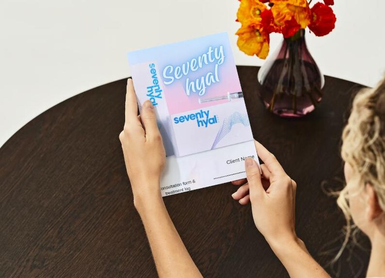May include: A blue and pink brochure with the text "Seventy Hyal" and a client name section. The brochure is being held by a person's hands.