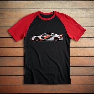 Op de afbeelding: Een zwart en rood t-shirt met een witte racewagen afbeelding op de voorkant. De auto is wit met zwarte en oranje accenten en het nummer 71 aan de zijkant.